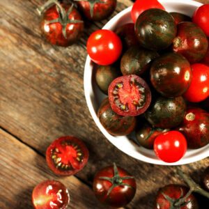 an abundance of Black Krim tomatoes in a white bowl on a wooden table