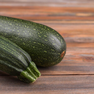 highlighting both ends of a black beauty zucchini that is sitting on a rustic wooden table
